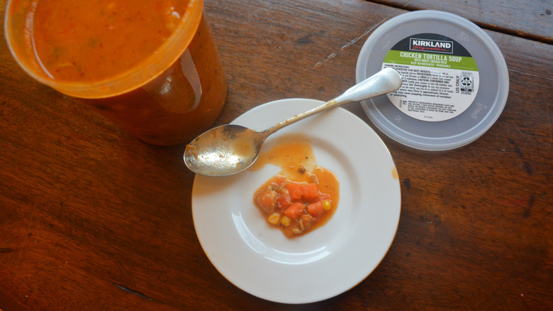 Some chicken tortilla soup is on a plate with a spoon and next to a soup container.