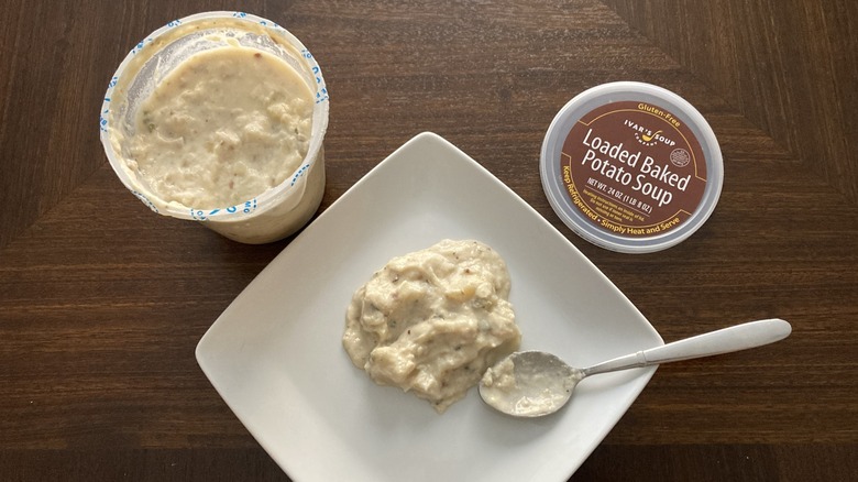 A bit of Ivar's Loaded Baked Potato Soup sits on a plate with a spoon next to a soup container.