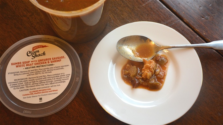 Some gumbo soup is on a plate with a spoon and next to a container of soup.