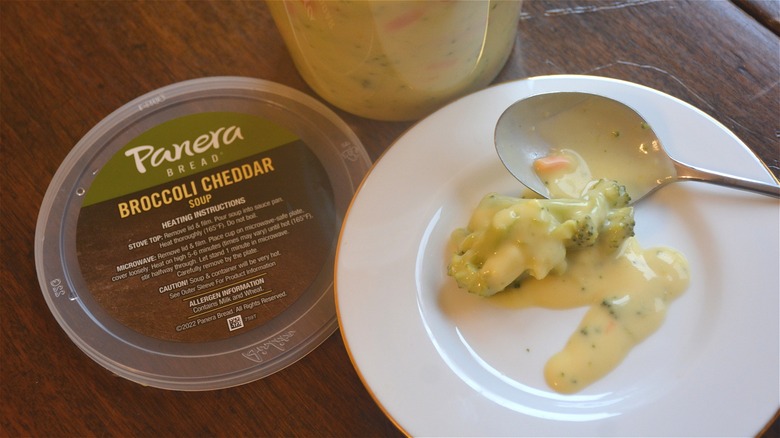 Some broccoli cheddar soup is on a plate with a spoon next to a soup container.