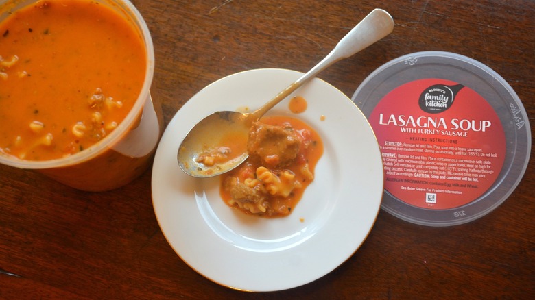 Some Blount's Lasagna Soup is on a plate with a spoon next to a soup container.