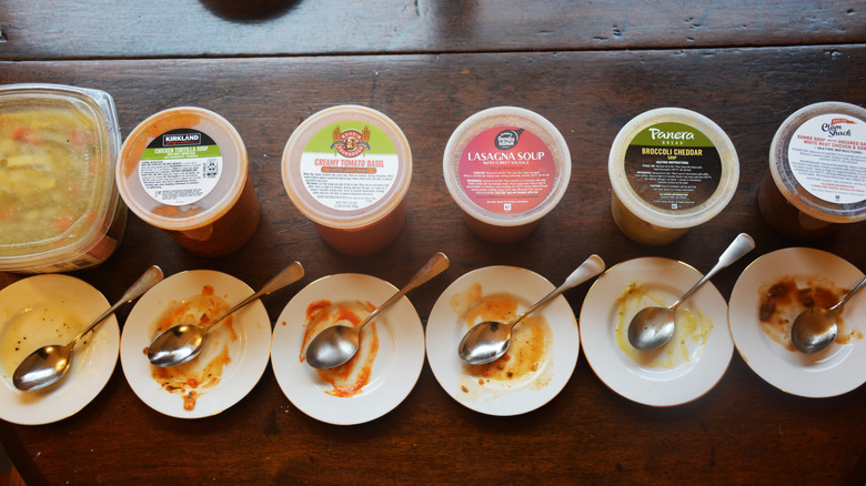 Tubs of soup and spoons are lined up on a table.