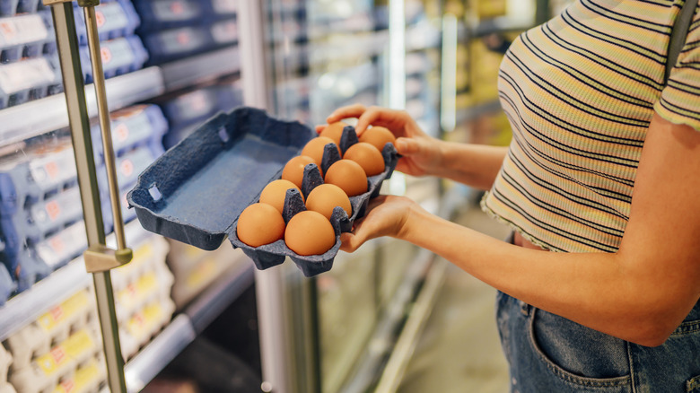 person inspecting carton of eggs at grocery store