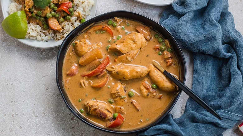 Chicken, peanut sauce, and veggies in black bowl.