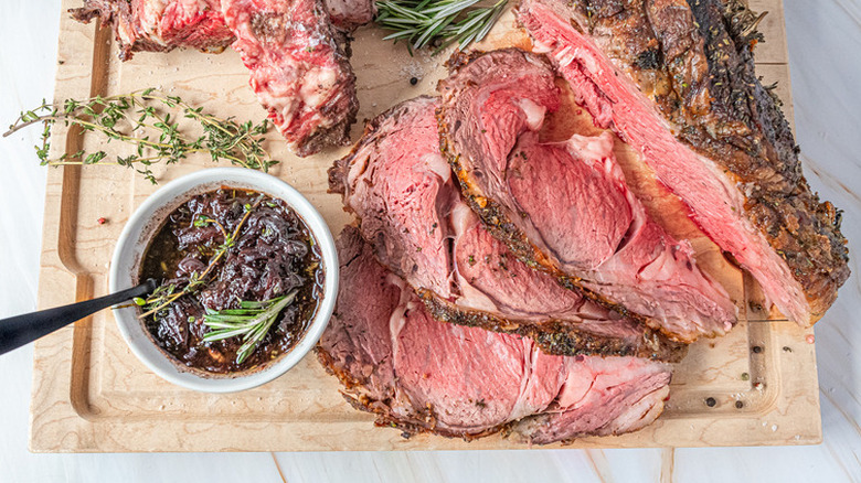 Sliced prime rib on board with herbs and sauce. 