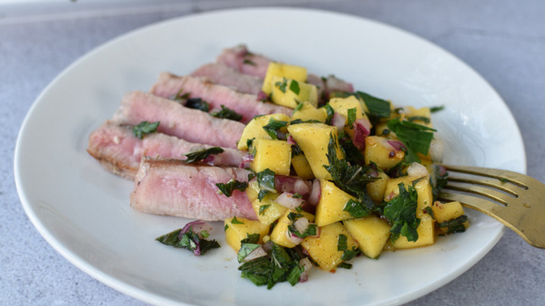 Sliced tuna steak with mango-mint salsa on plate. 