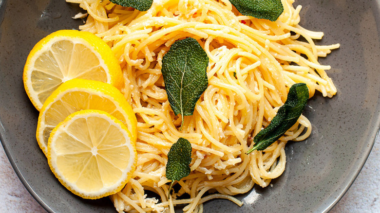 Cooked spaghetti with lemon slices and sage leaves.