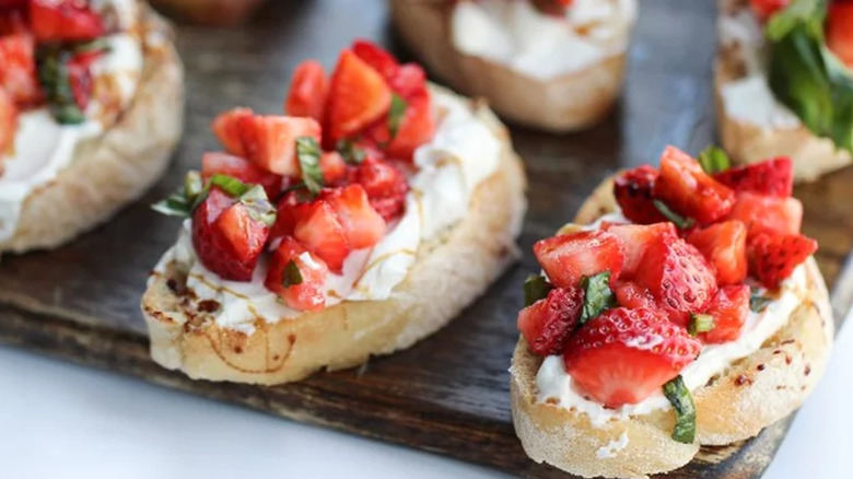 Bread slices with berries, basil strips, and cheese.