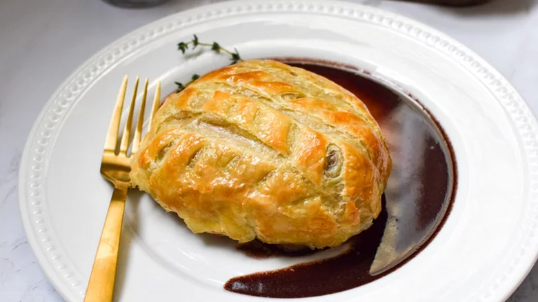 Pastry-wrapped beef on plate in pool of gravy.