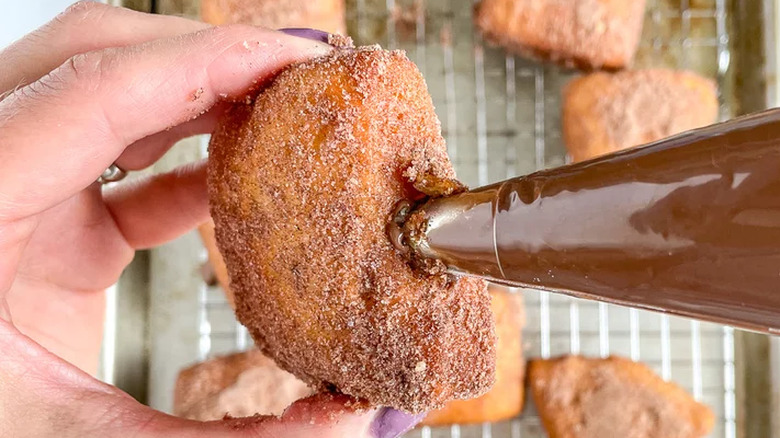Hand holding donut while filling with chocolate.