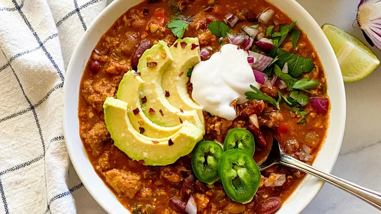 Large bowl of chili with avocado slices, jalapenos, and cream.