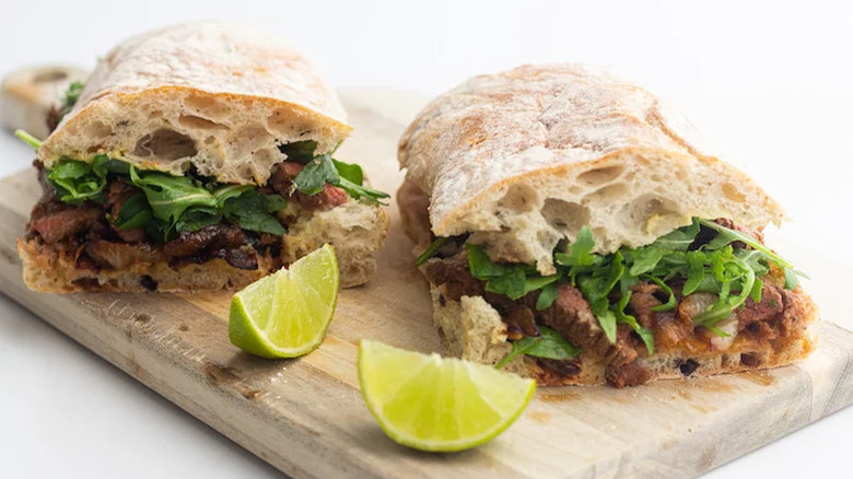 Ciabatta sandwiches with steak, greens, and lime wedges.