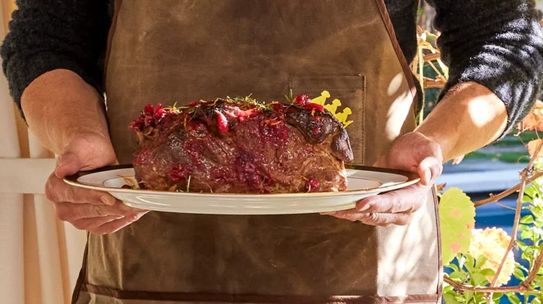 Person holding a pork shoulder in a plate