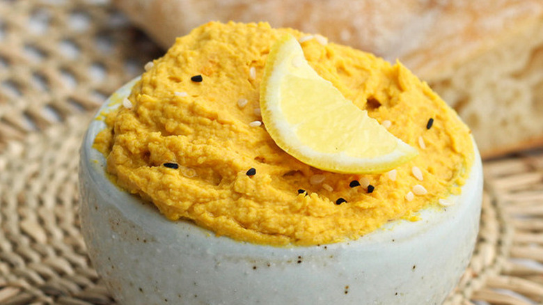 Small bowl of creamy pumpkin hummus with lemon wedge.