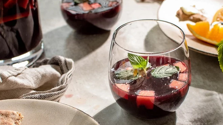 Glass of red sangria with apple cubes and mint.