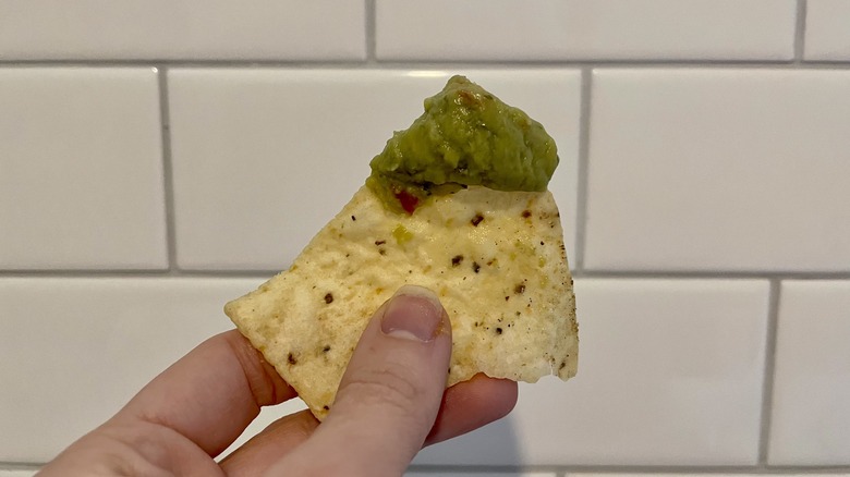 Hand holding chip with guacamole 