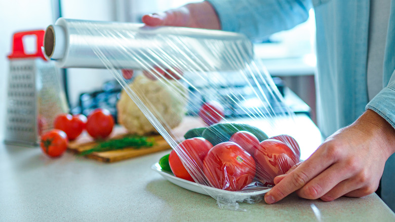 Person holding roll of plastic wrap over tomatoes