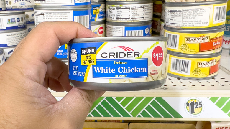 Hand holding can of chicken in grocery store