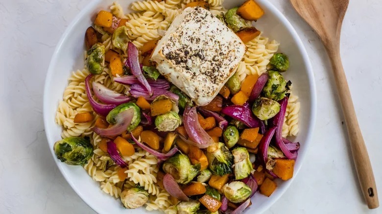 bowl of baked feta pasta with roasted veggies and wooden spoon