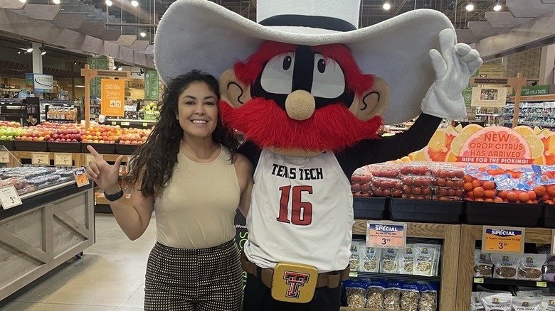 Person posing with mascot in Market Street produce department