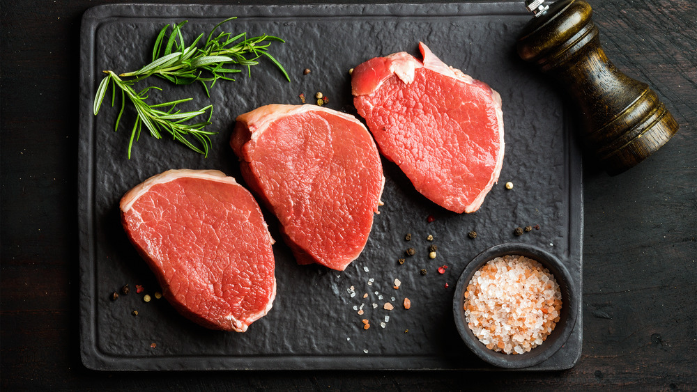 Round steaks on black stone board