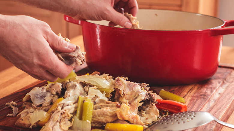 hands separating the chicken meat from bones