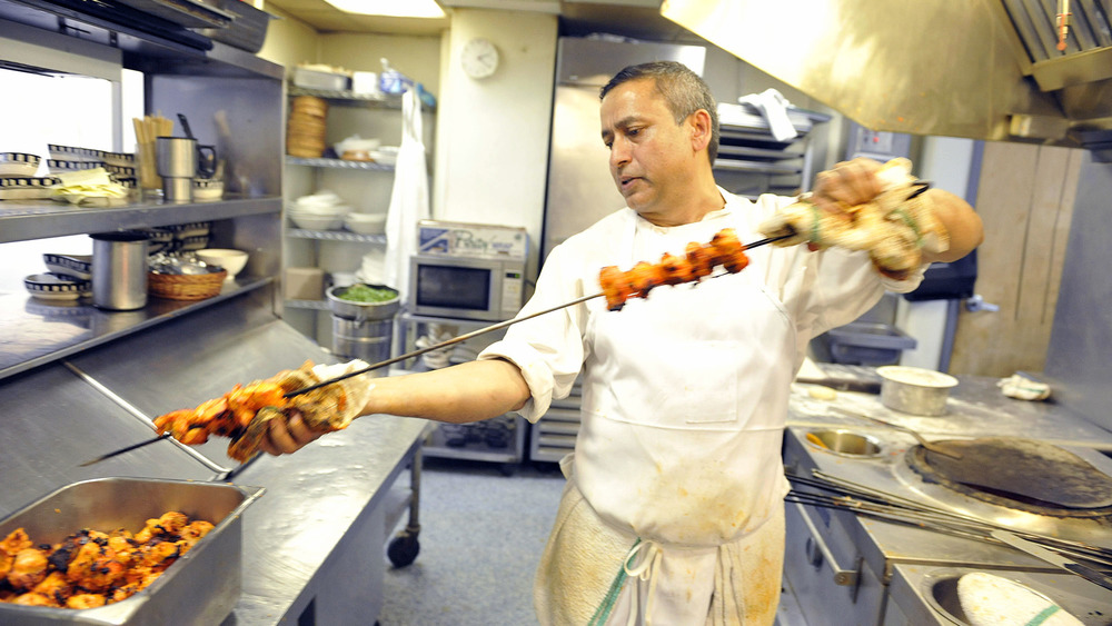 CA chef putting chicken on a skewer