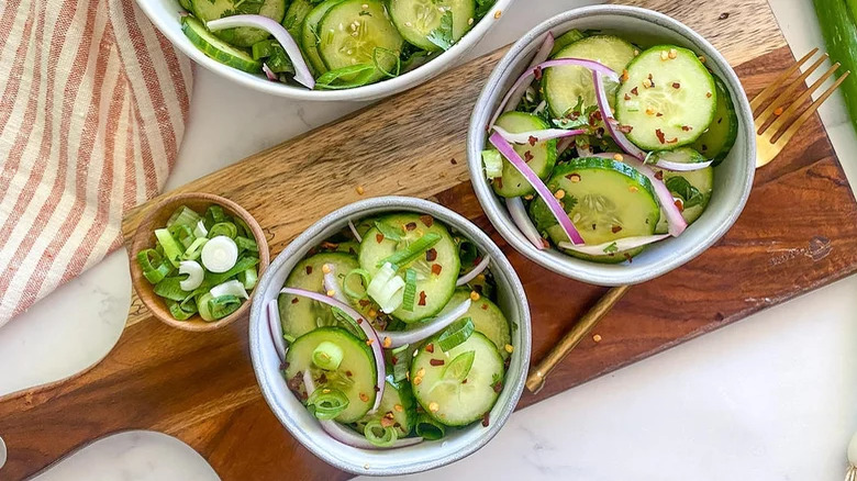 bowls of asian cucumber salad on wooden cutting board