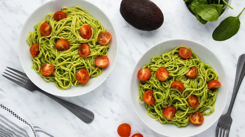 bowls of creamy avocado pasta with tomatoes forks