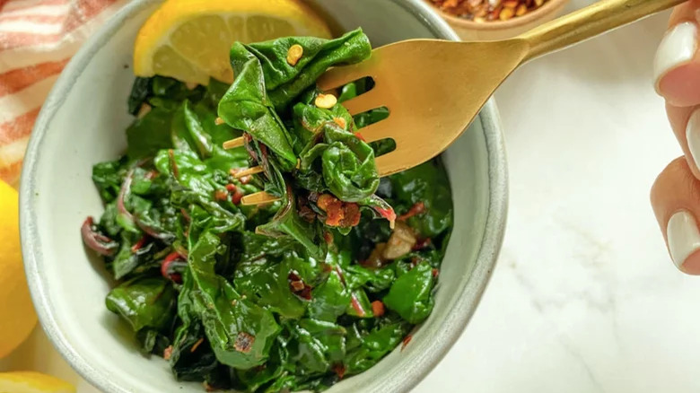 bowl of sauteed swiss chard with fork and lemon slice