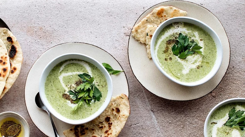bowls of cream of broccoli soup with pita bread on side