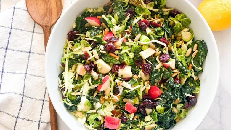 bowl of sweet kale salad with wooden spoon on side