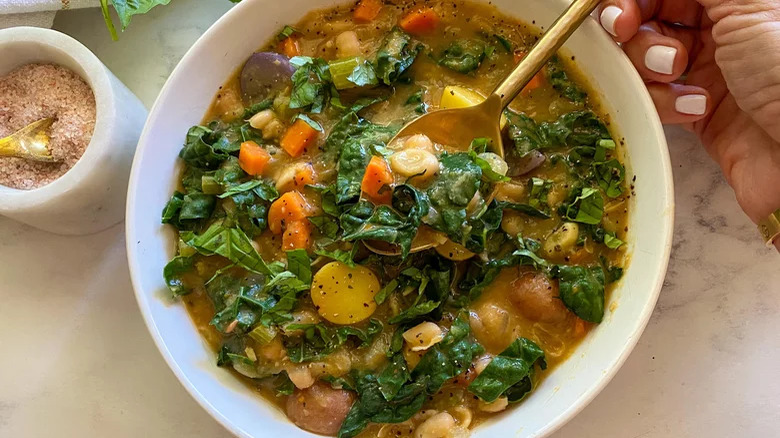 hand with spoon in bowl of white bean and kale soup