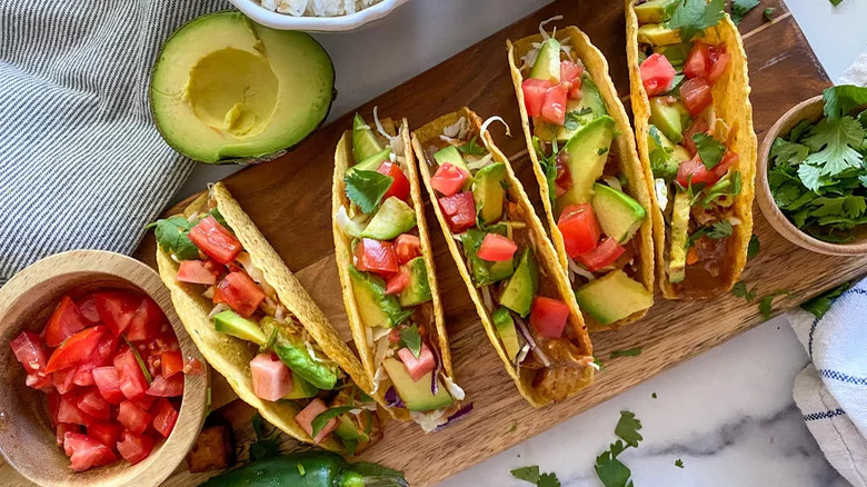 wooden board with spicy thai tofu tacos avocado tomatoes cliantro