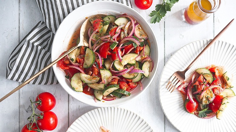 bowls of cucumber tomato salad with utensils and dish towel