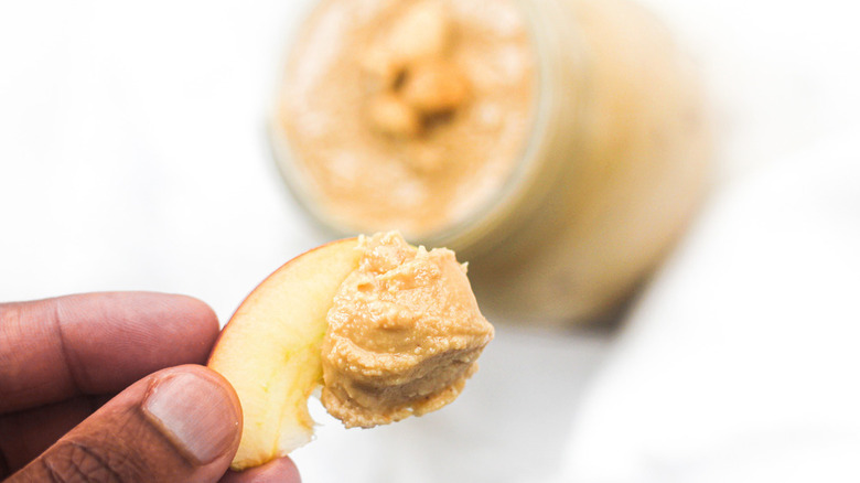 hand holding apple with homemade peanut butter with jar in background