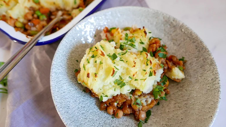 bowl of vegan shepherd's pie with casserole dish and spoon