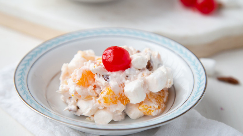 A bowl of fruit ambrosia with marshmallows and a cherry on top