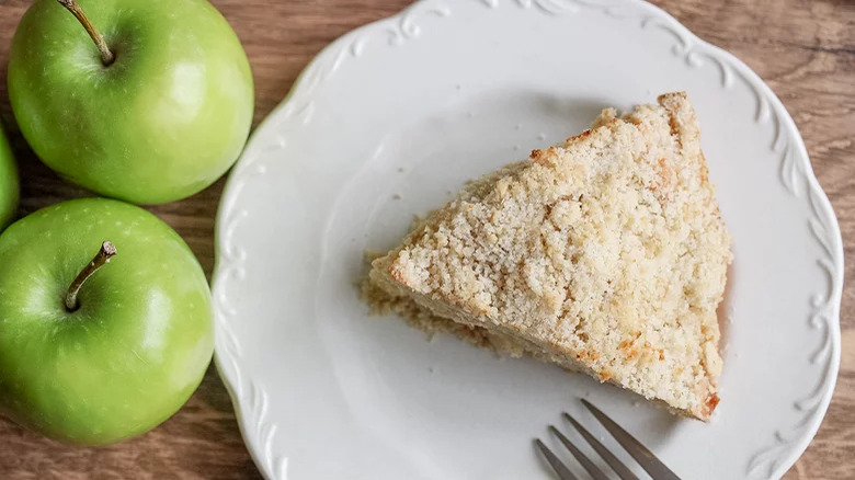 A slice of apple cake with green apples on the side