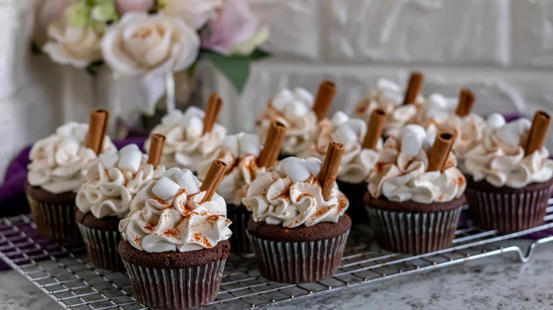 Cupcakes with whipped cream and cinnamon sticks on a wire rack