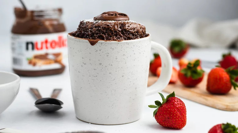 A mug cake with Nutella and strawberries in the background