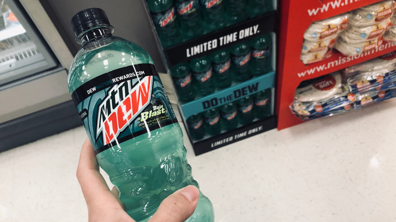 A person holding a bottle of Mtn Dew baja blast