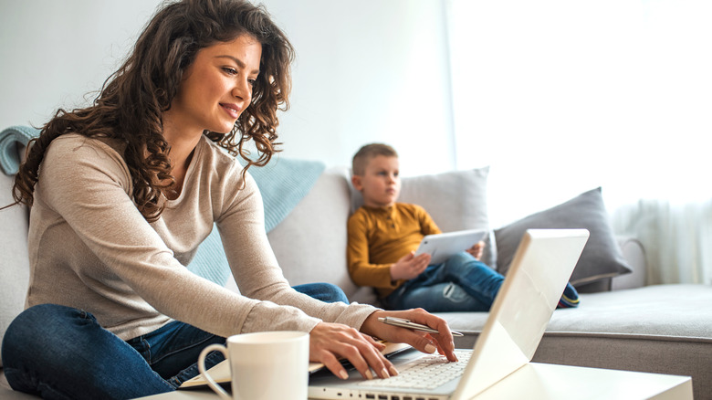 Parent on laptop with child in background