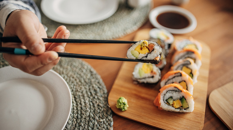 Hand holding sushi with chopsticks