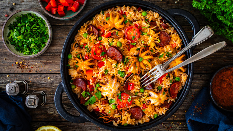 seafood and chorizo paella on a wood table with small bowls of ingredients