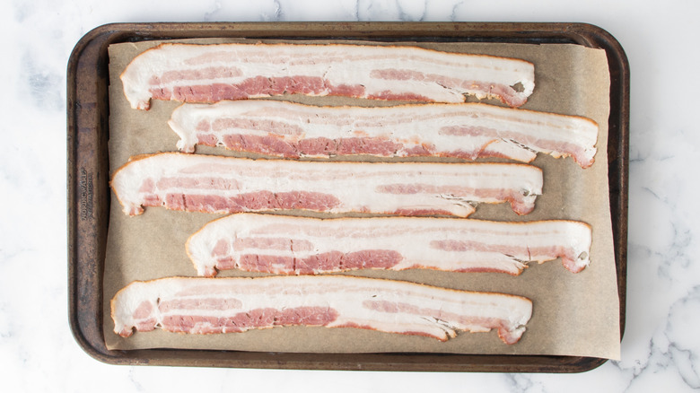 raw bacon strips in a metal baking pan lined with paper