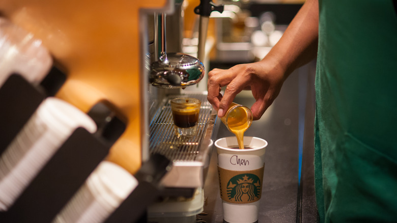 Starbucks barista in green apron pouring a shot