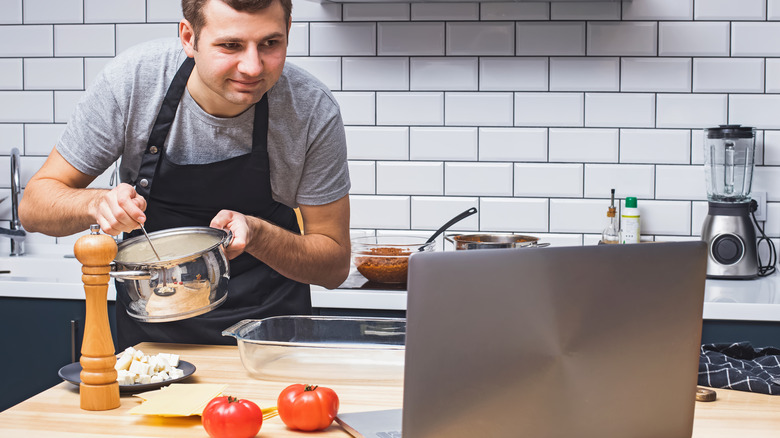 Man cooking while looking at laptop