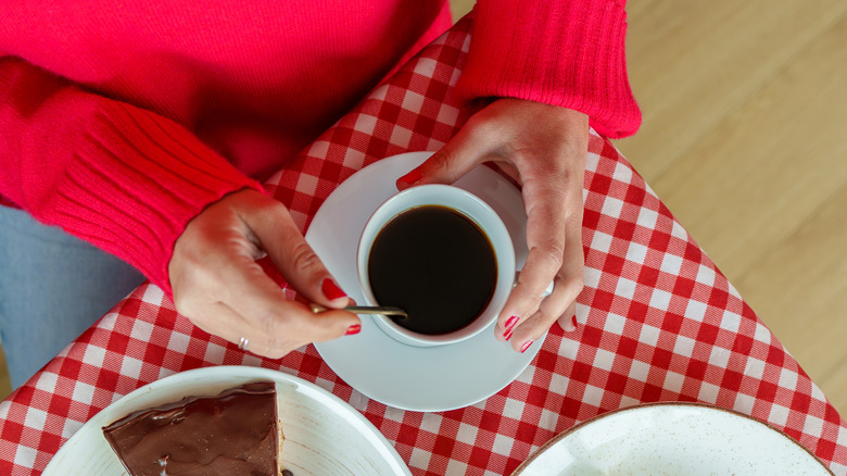 Person with red nails in red sweater stirring cup of coffee