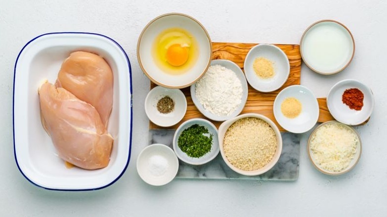 three bowls with a flour mixture, egg mixture, and seasonings along with a platter of raw chicken bites